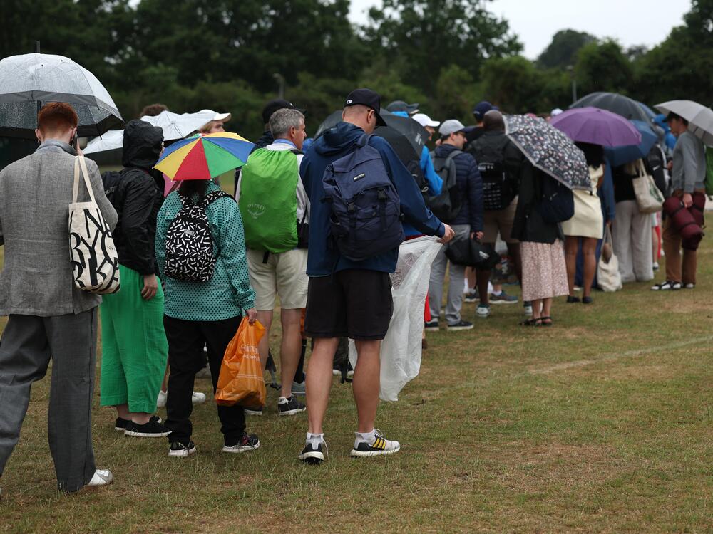 Spectators queue under umbrellas as it rains on day three at Wimbledon, July 2.