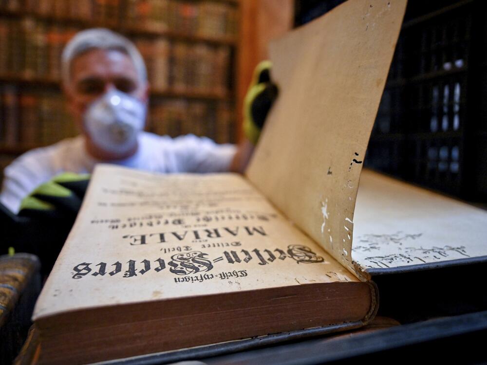 In this photo provided by Pannonhalma Archabbey, a restorer shows an old book with holes in its pages due to a drugstore beetle infestation, at the Pannonhalma Archabbey's library in Pannonhalma, Hungary on July 3.