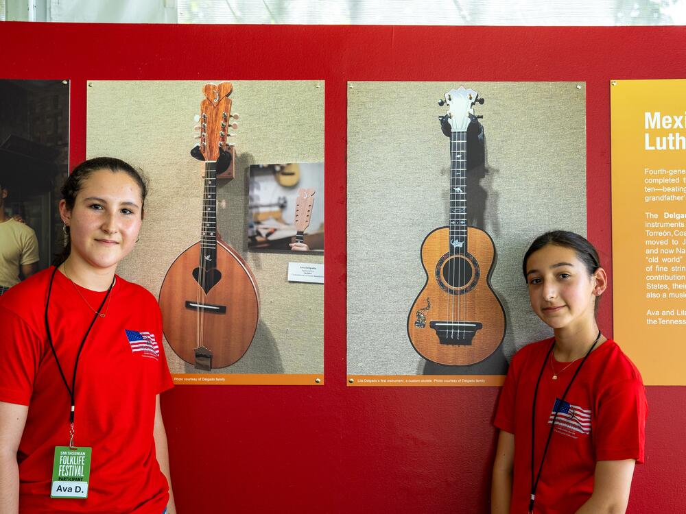 Sisters Ava, left, and Lila Delgado stand next to a photograph of the instruments they made by hand under the tutelage of their father, Manuel Delgado.