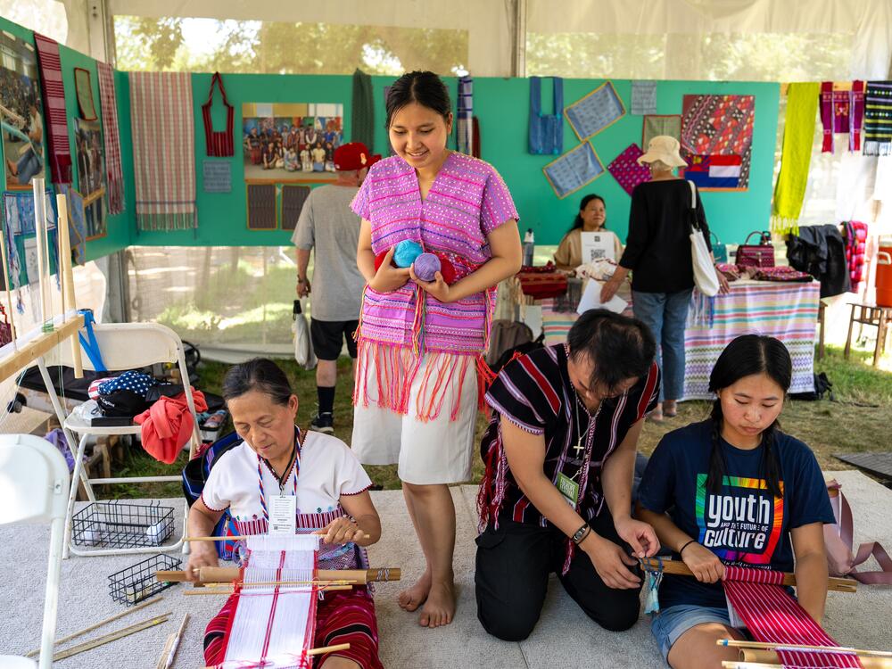 Rosie Say (seated left) weaves a bag. Her weaving student Ku Say stands by her side. They are joined by members of the Karen Weaving Circle, a group of multigenerational refugee weavers.