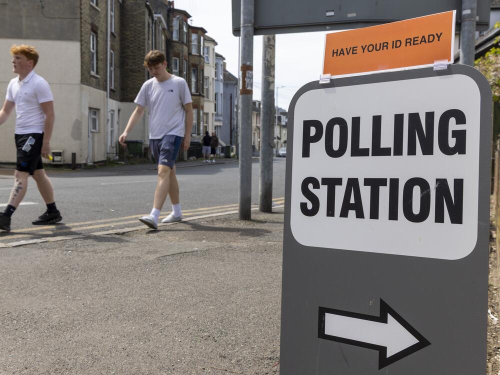 People walk past a sign for a polling station during local council elections in Folkestone, England in May. The British government is announcing plans to lower the voting age to 16.