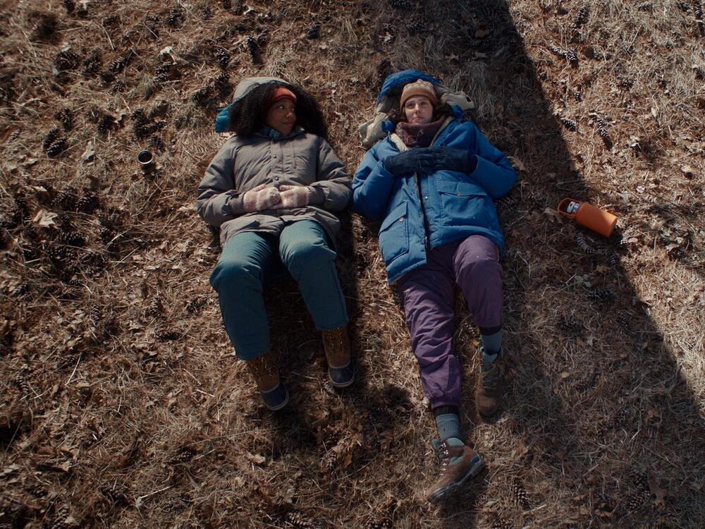 Lydie, played by Naomi Ackie (left), lays on the ground next to Agnes (Eva Victor) in this still from <em>Sorry, Baby</em>.