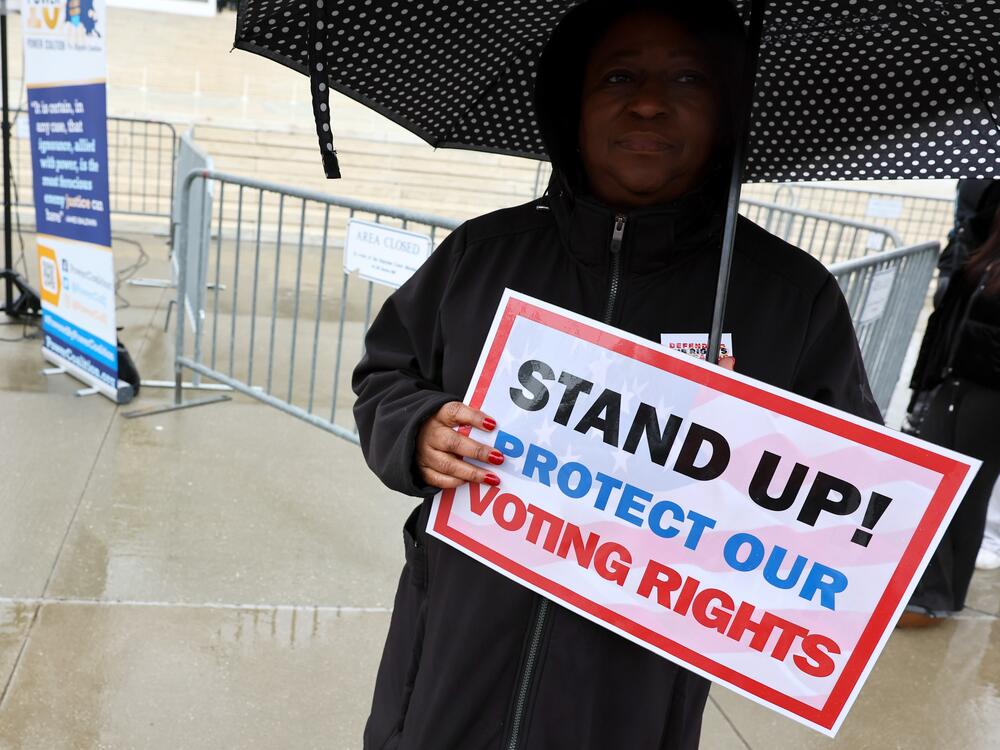 A demonstrator holds an umbrella and a sign saying 