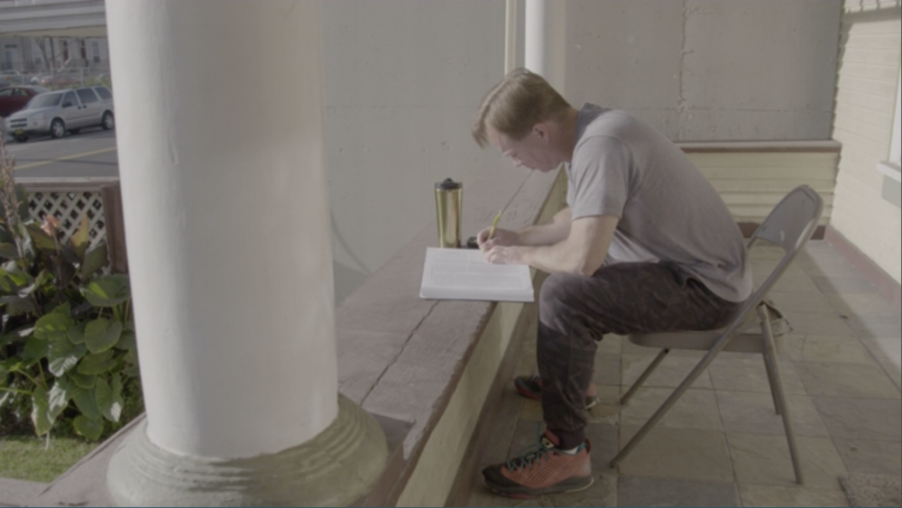 A person sits in a folding chair and writing in a book.