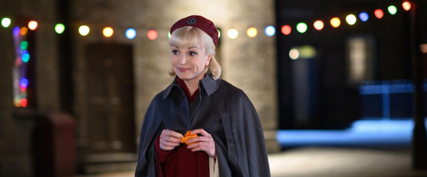 Nurse Trixie in uniform on a street lit with Christmas lights.