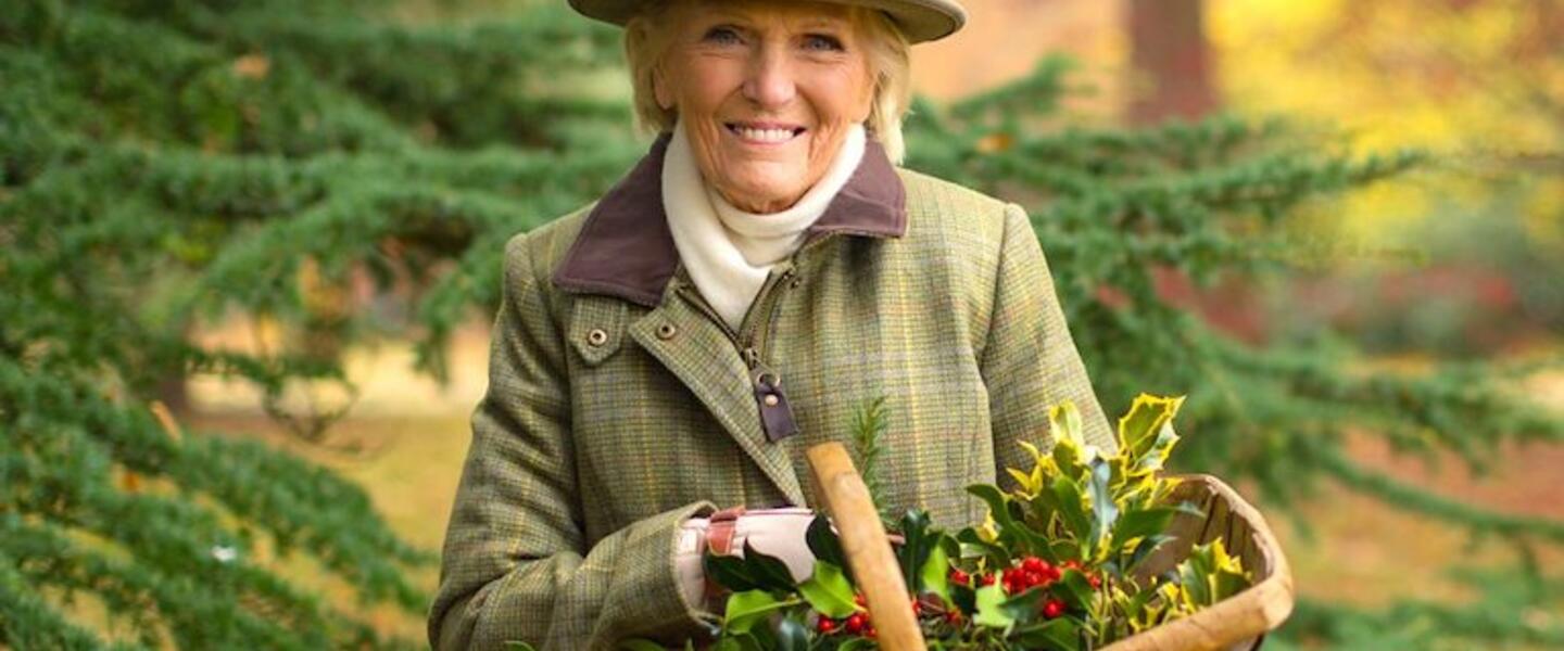 Mary Berry holding a basket of holly outdoors.