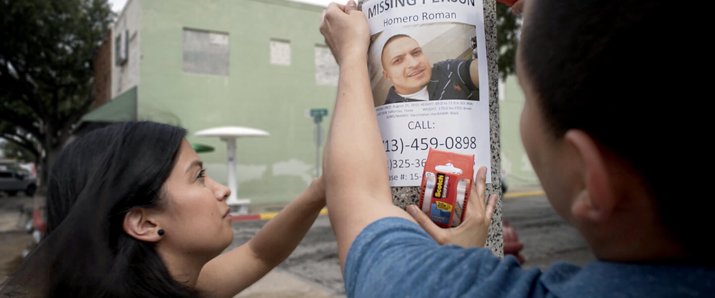 A man and woman put up a missing person poster.