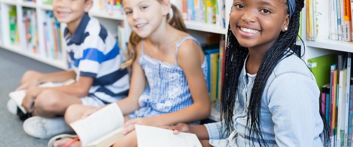 Children seated inside of a library, holding books and smiling.