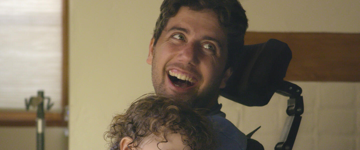 A man in a wheelchair holds his young son.