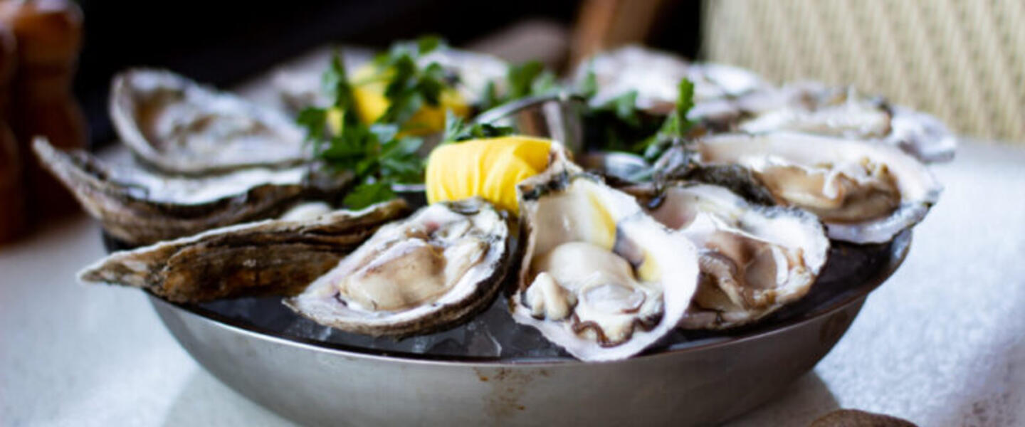 A plate of fresh, raw oysters with lemon and parsley sits on a table at C&S Seafood & Oyster Bar.