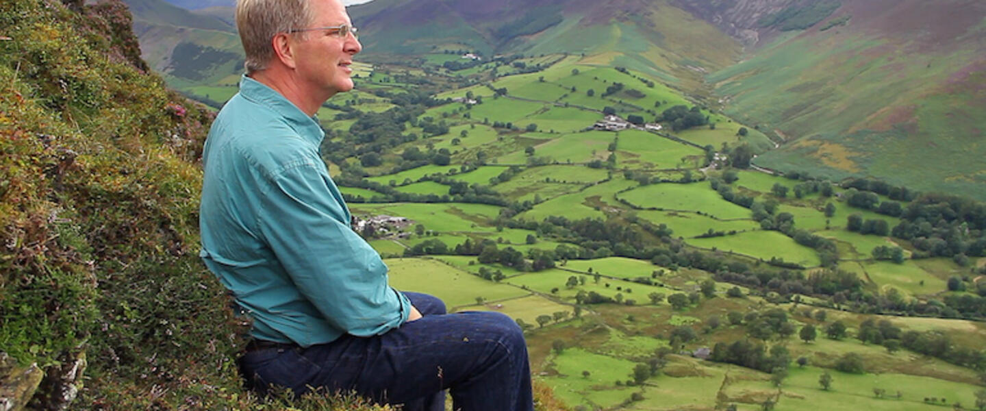 Rick Steves sitting on a mountainside.