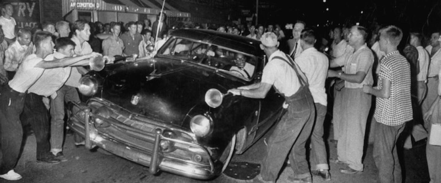 A group of white men attack a car driven by a black man in the 50s.