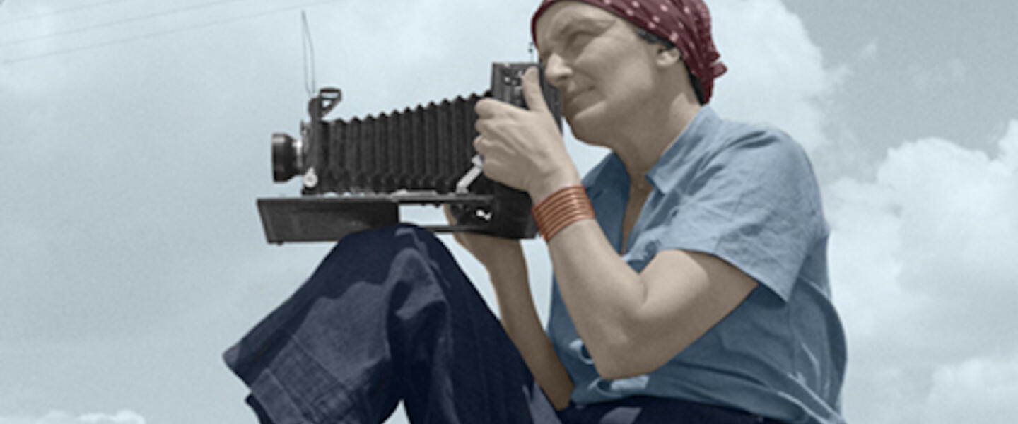 An old photograph of a woman taking a picture with an antique camera.