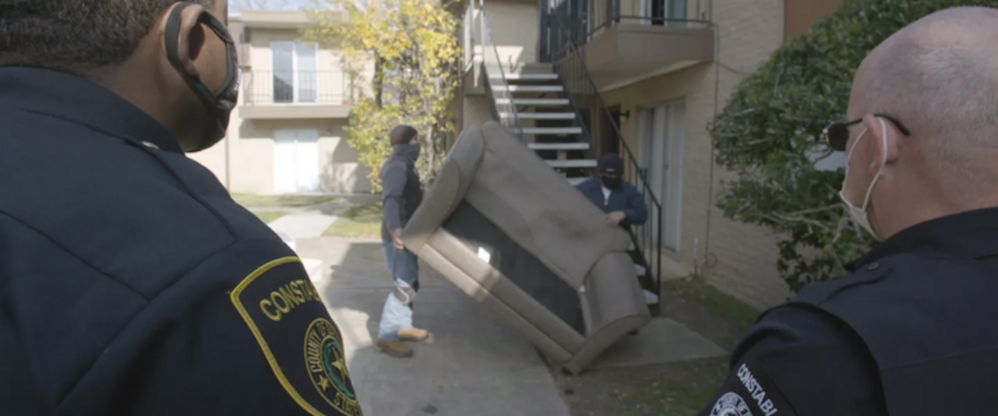 2 police officers watch as men carry a couch down a set of stairs.
