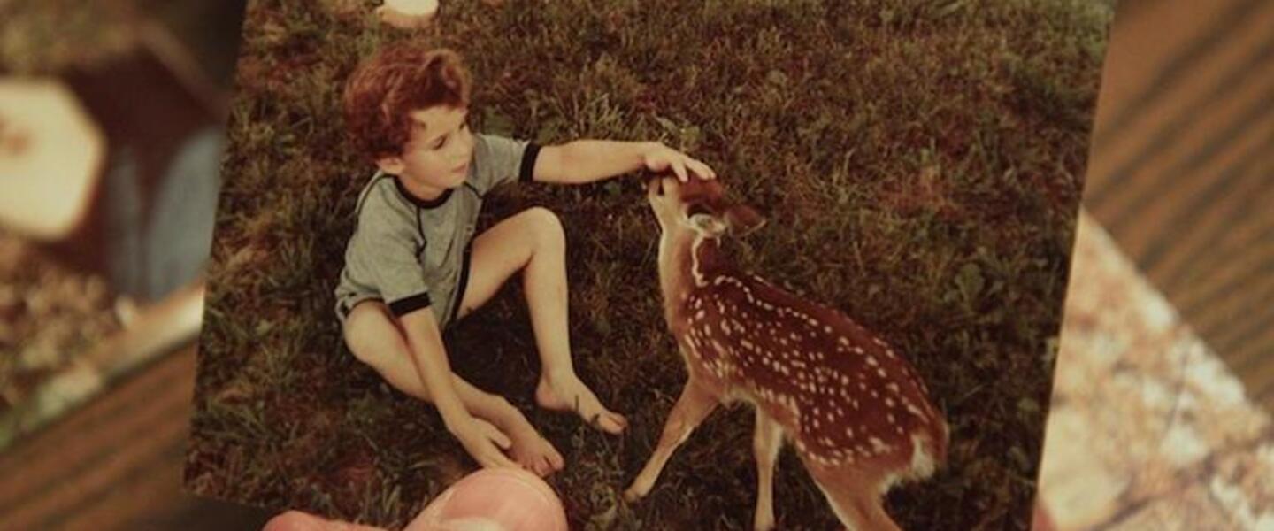 A person holds a picture of a child petting a fawn.
