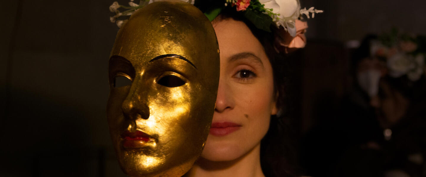 A woman's face is half obscured by a golden mask.