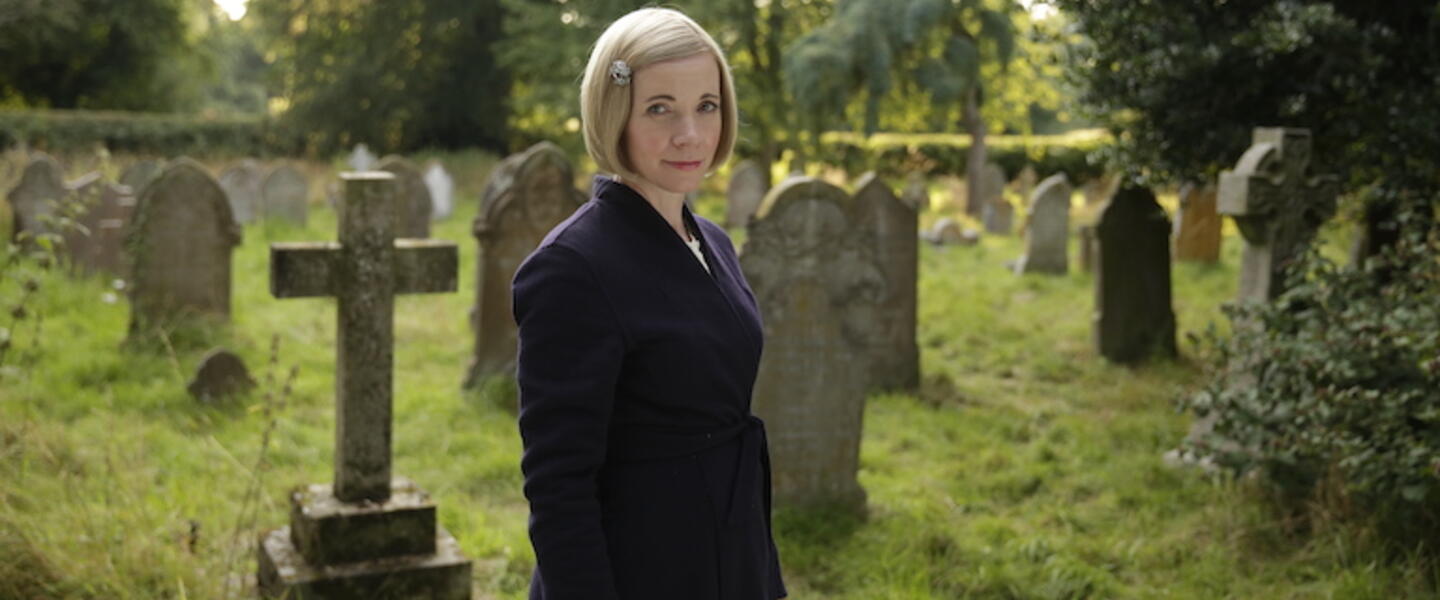 Lucy Worsley standing in an old graveyard.