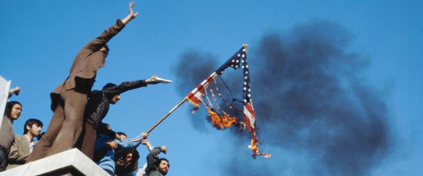 Men stand on a roof with a burning American flag.