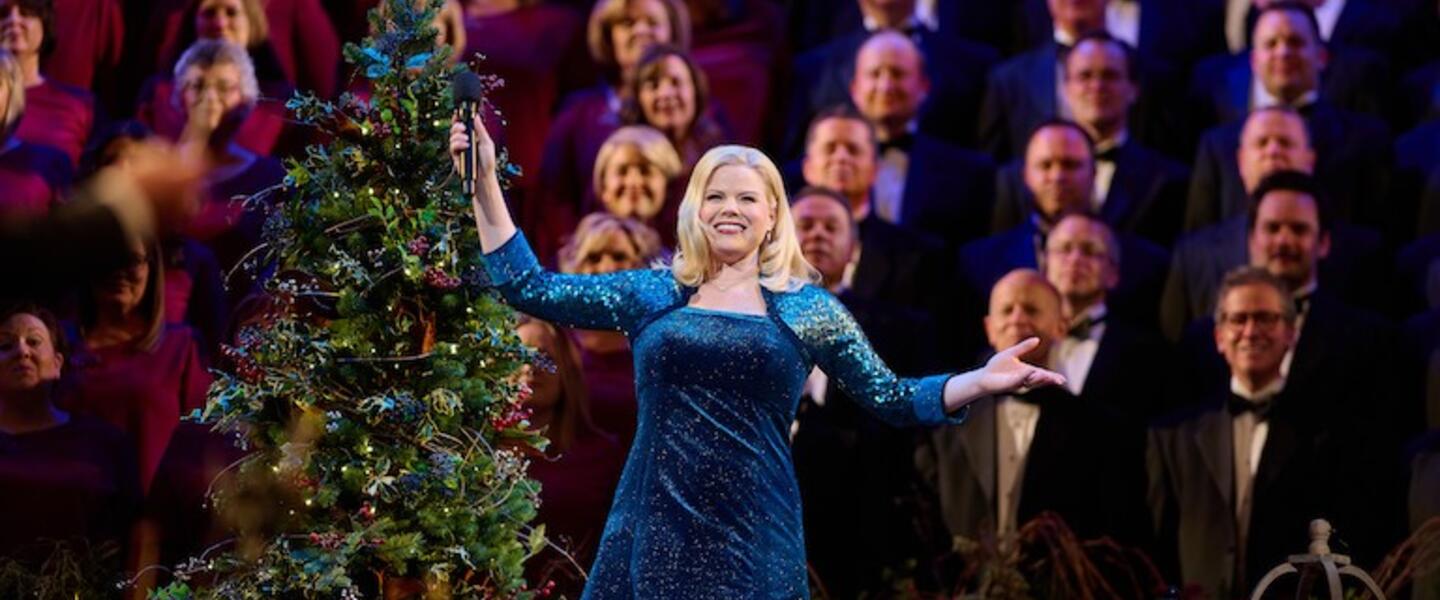 A woman in a blue gown standing in front of a choir and Christmas tree.