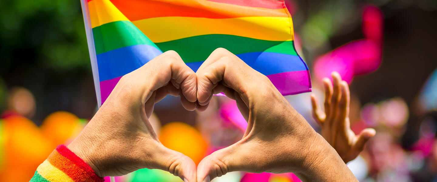 Love symbol with hands in front of a pride flag