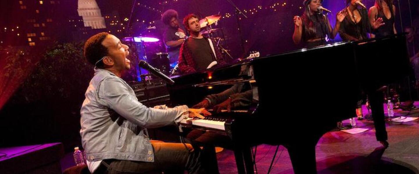 John Legend on stage singing and playing piano.