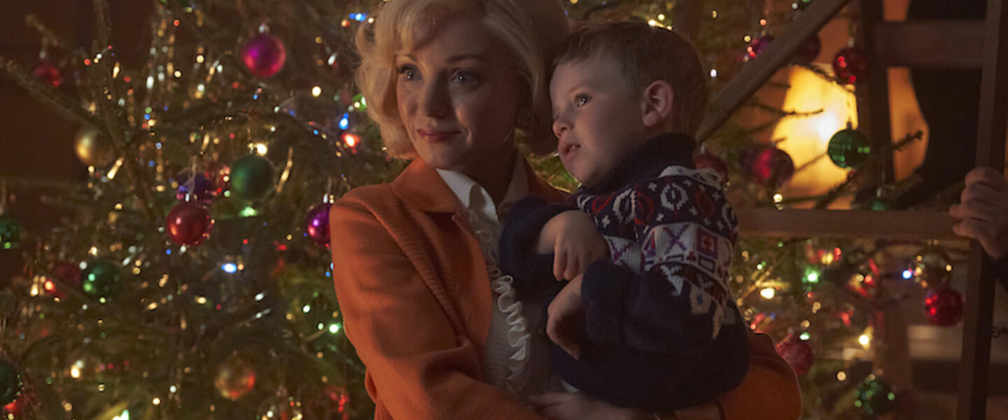 Trixie from Call the Midwife holding a child in front of a Christmas tree.