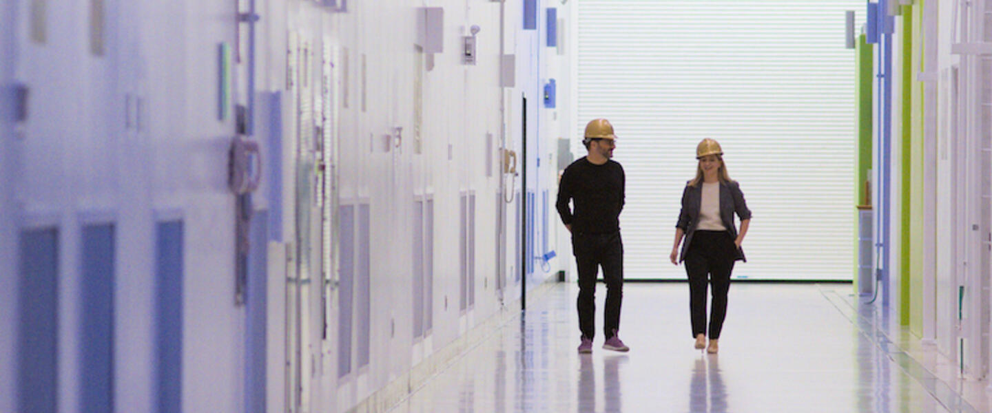 A man and woman in hardhats walking down a sterile corridor.