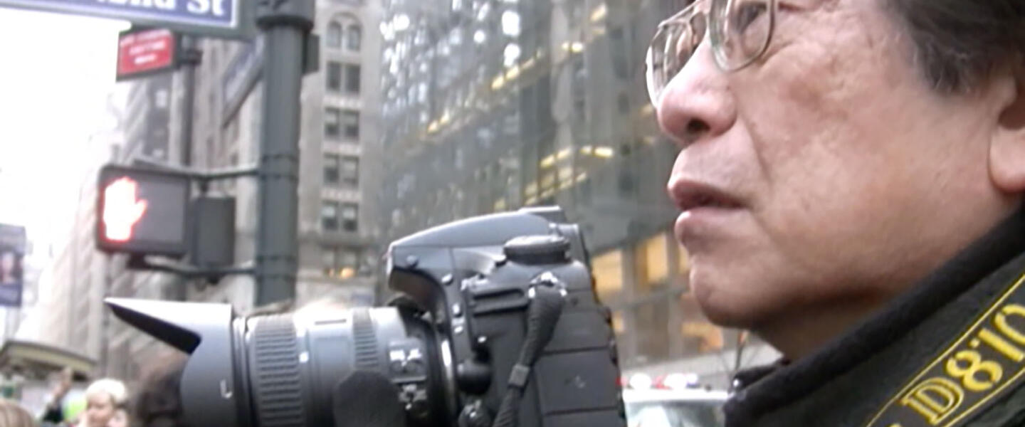 Photographer Corky Lee holding a camera on 42nd Street in Manhattan.