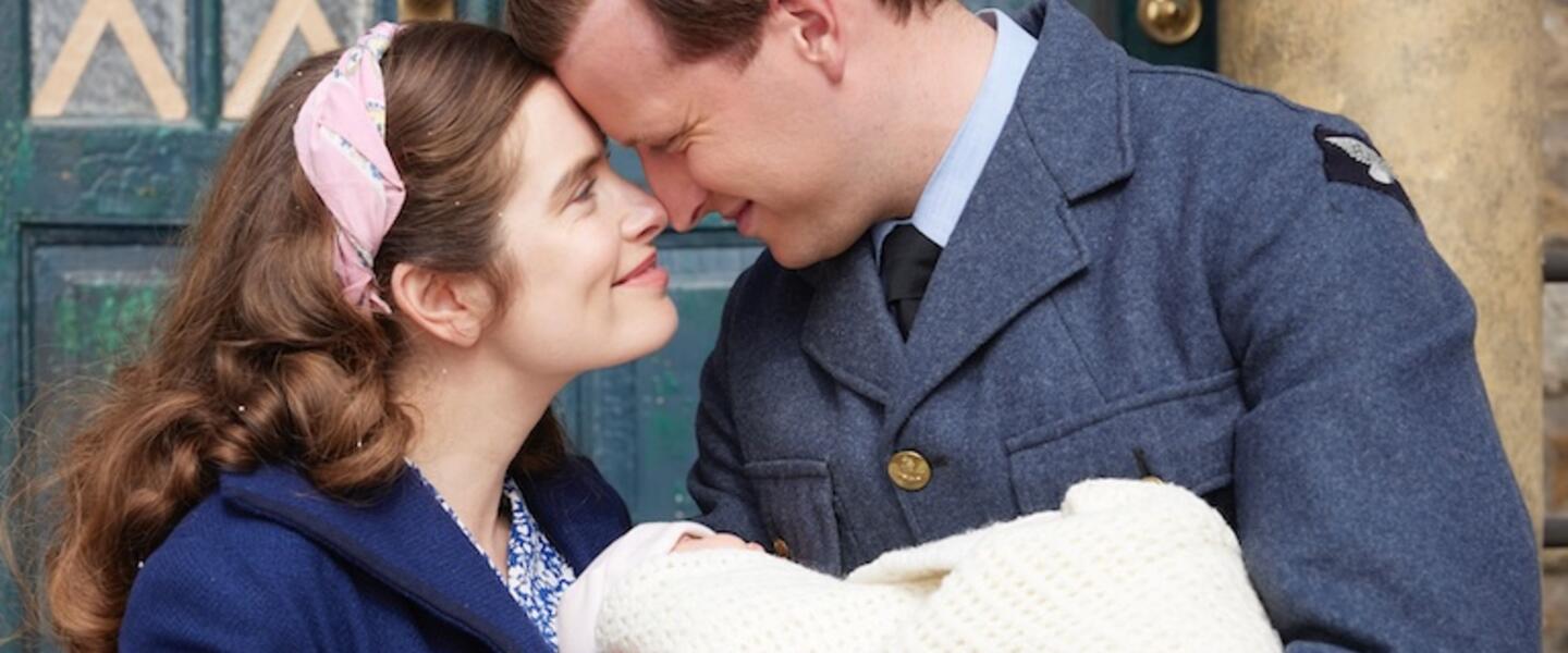 A young couple embrace with their infant in a doorway.