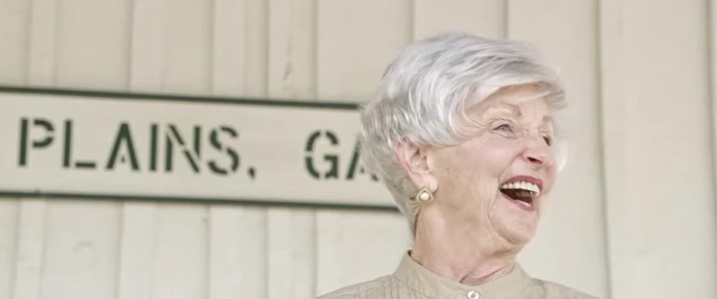 An elderly woman standing on a train platform.