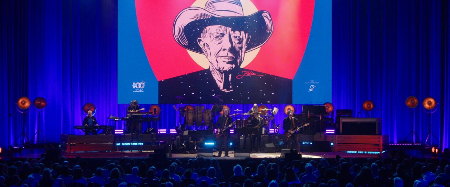 A performer on stage in front of an image of President Jimmy Carter.