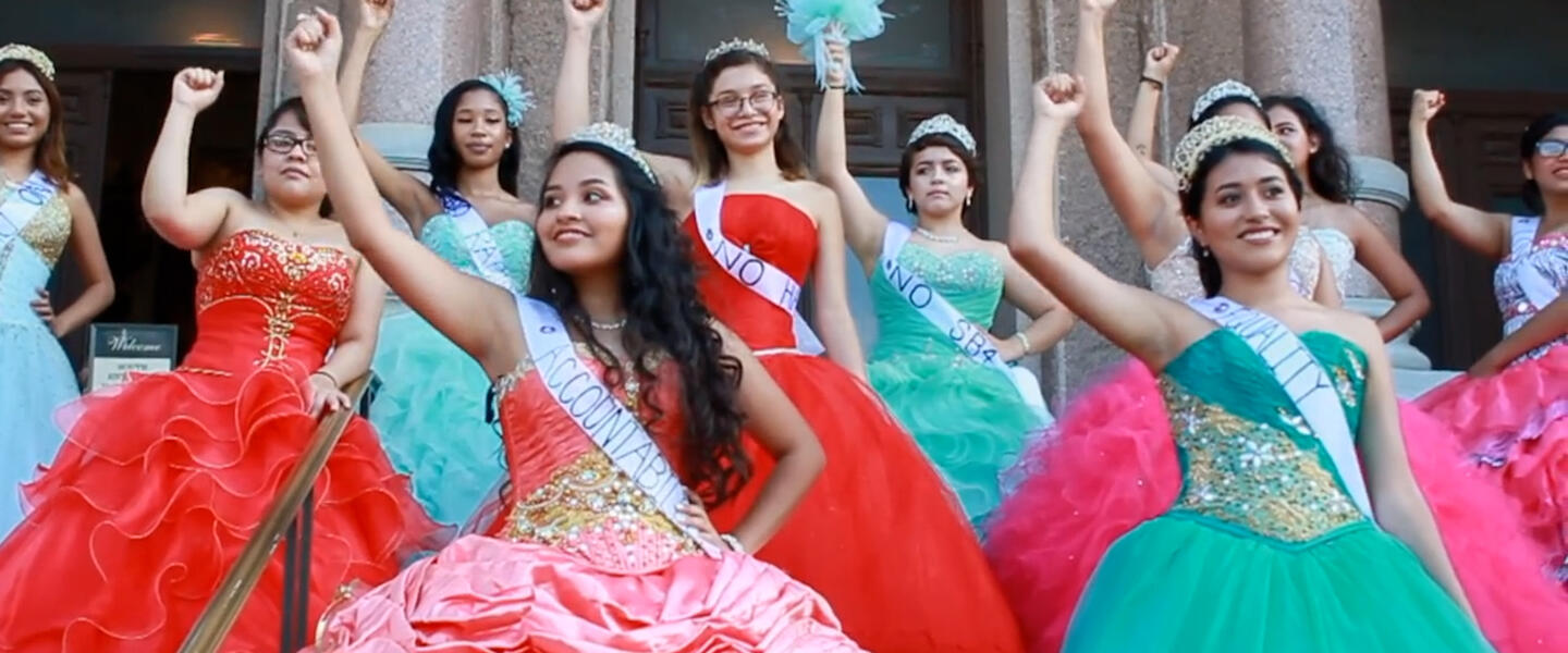A group of teenage girls in dresses raising their fists.