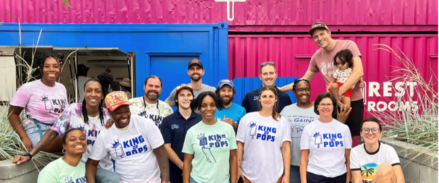 A crew of people wearing King of Pops t-shirts stand in front of a King of Pops storefront.