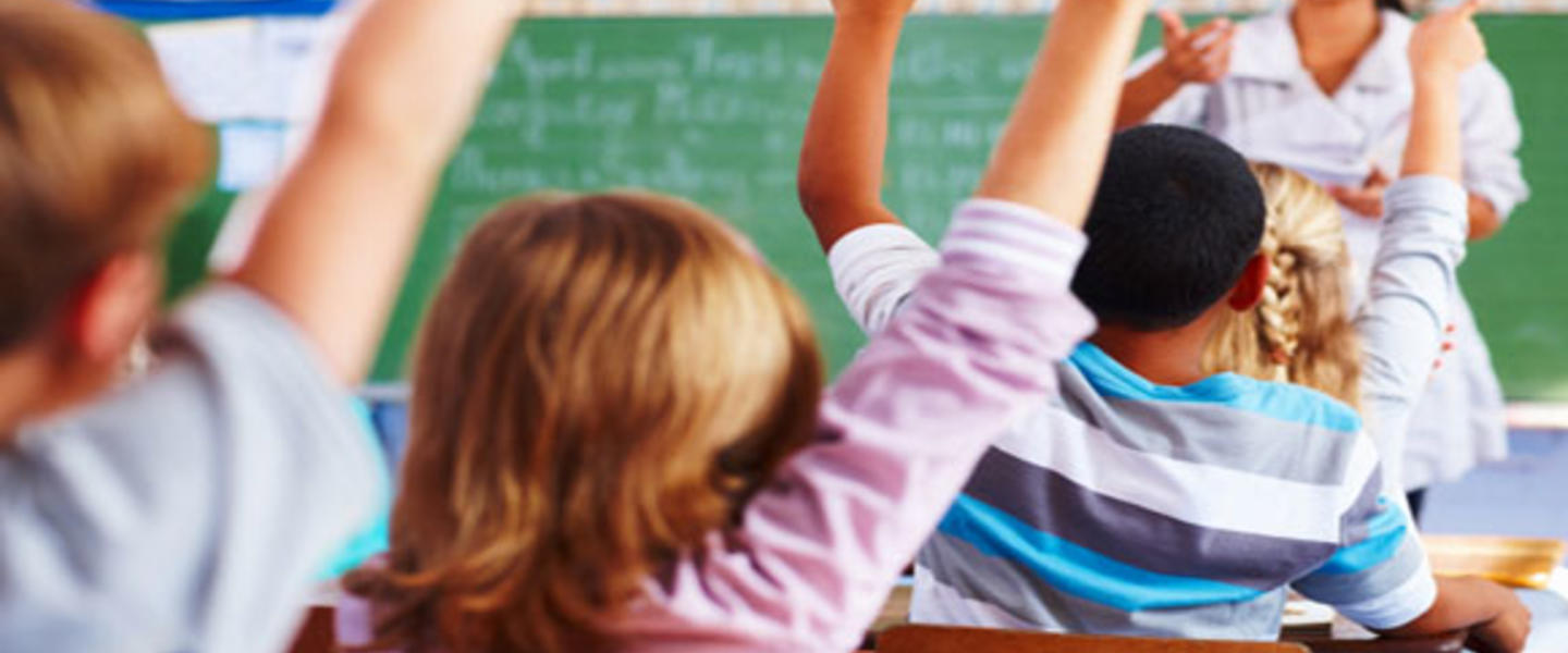 Children raising their hands in a classroom.