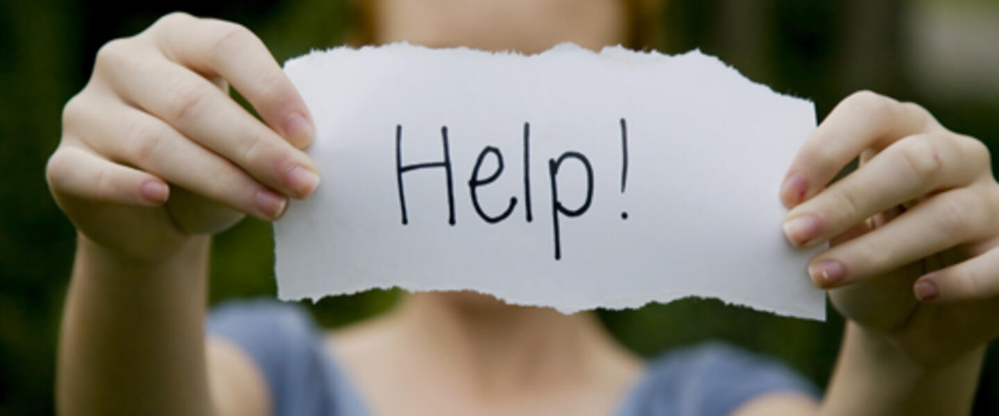 A young person holds a scrap of paper with the word "Help!" written on it