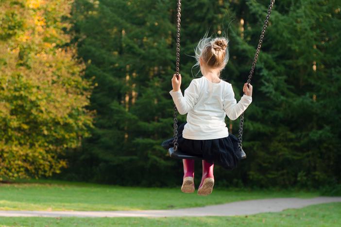 A child wearing pink rain boots uses a swing