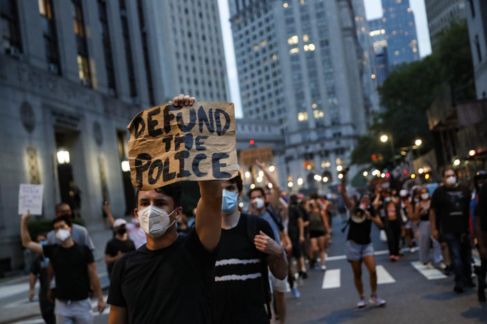 A man at a protest holds a sign that reads "Defund the Police."