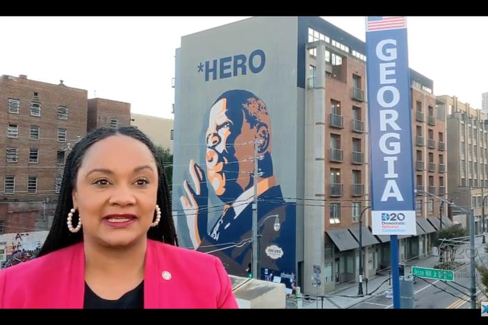 Georgia Democrats Nikema Williams stands aside a mural of John Lewis.