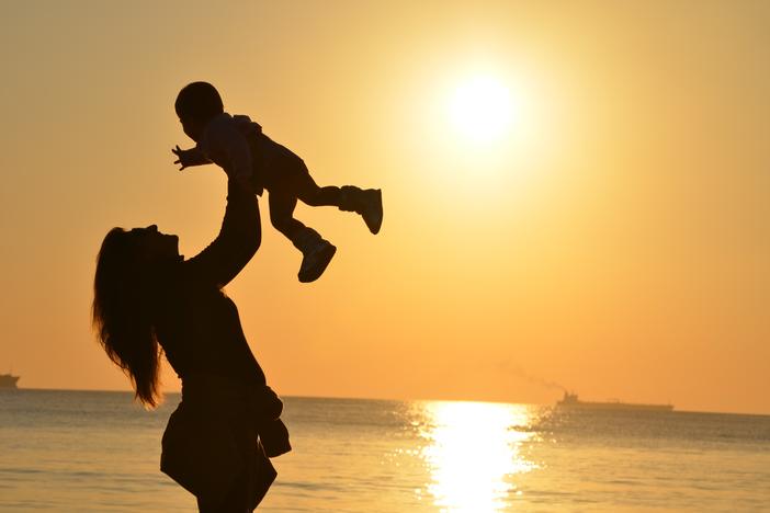 A person holds a toddler up on a beach