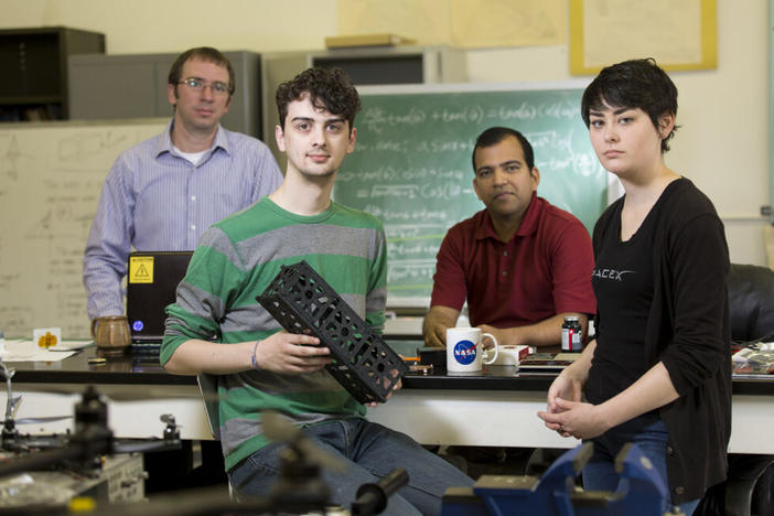 Post Doc research scientist David Cotten of the Center for Geospatial Research, Senior computer science and astrophysics major Caleb Adams, Professor of Geography Deepak Mishra, and senior mechanical engineering major Megan Le Corre are working together along with a team of students and professors in a collaborative effort to design, build, and deploy (with the help of NASA) a cube satellite. Adams is holding a 3D printer model of the CubeSat,