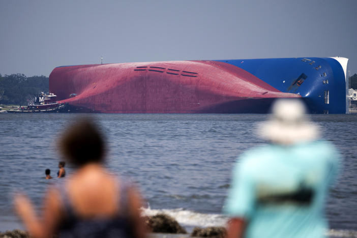 Visitors to Driftwood Beach watch a Moran tugboat near the stern of the vessel Golden Ray as it lays on its side as a tent and rescuers can be seen near the bottom of the ship near the tug boat, Monday, Sept. 9, 2019, in Jekyll Island, Georgia. Coast Guard rescuers had made contact with four South Korean crew members trapped inside a massive cargo ship off the coast of Georgia. All four were rescued. (AP Photo/Stephen B. Morton)