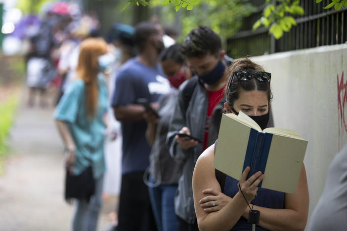 Kelsey Luker reads as she waits in line to vote, Tuesday, June 9, 2020, in Atlanta. Luker said she had been in line for almost two hours. 