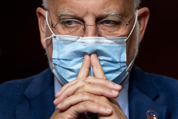 Dr. Robert Redfield wears a mask with his hands in front of his mouth.