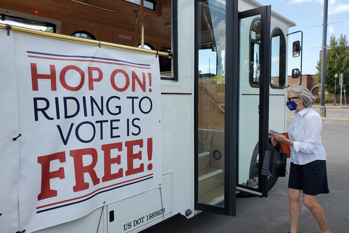 Rebecca Rolfes boards a trolley, which holds a banner announcing "riding to vote is free"