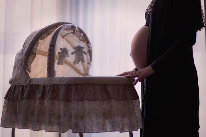 A pregnant woman stands next to a crib.