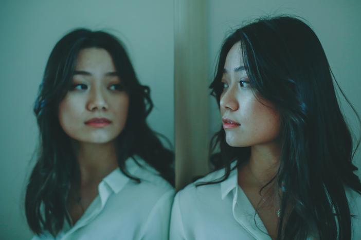 An Asian woman looks at her reflection in the mirror