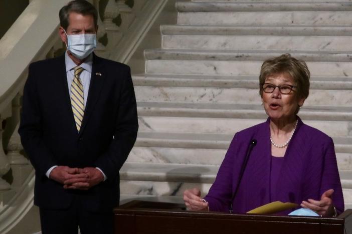 Dr. Kathleen Toomey speaks at a press conference with Governor Brian Kemp standing nearby.