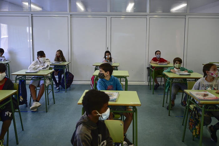 Students wearing masks sit at rows of desks in a classroom.