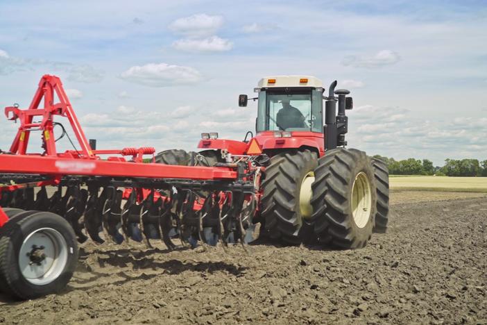 Tractor tills soil on farmland.