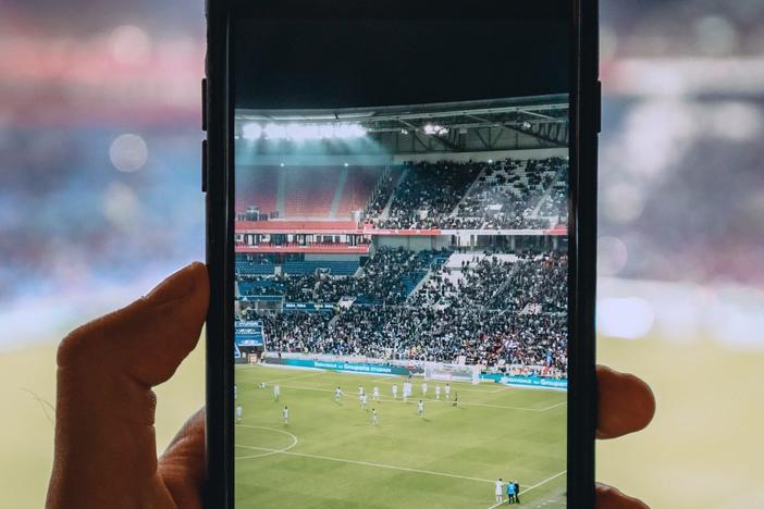 Person taking photo with cell phone at football game